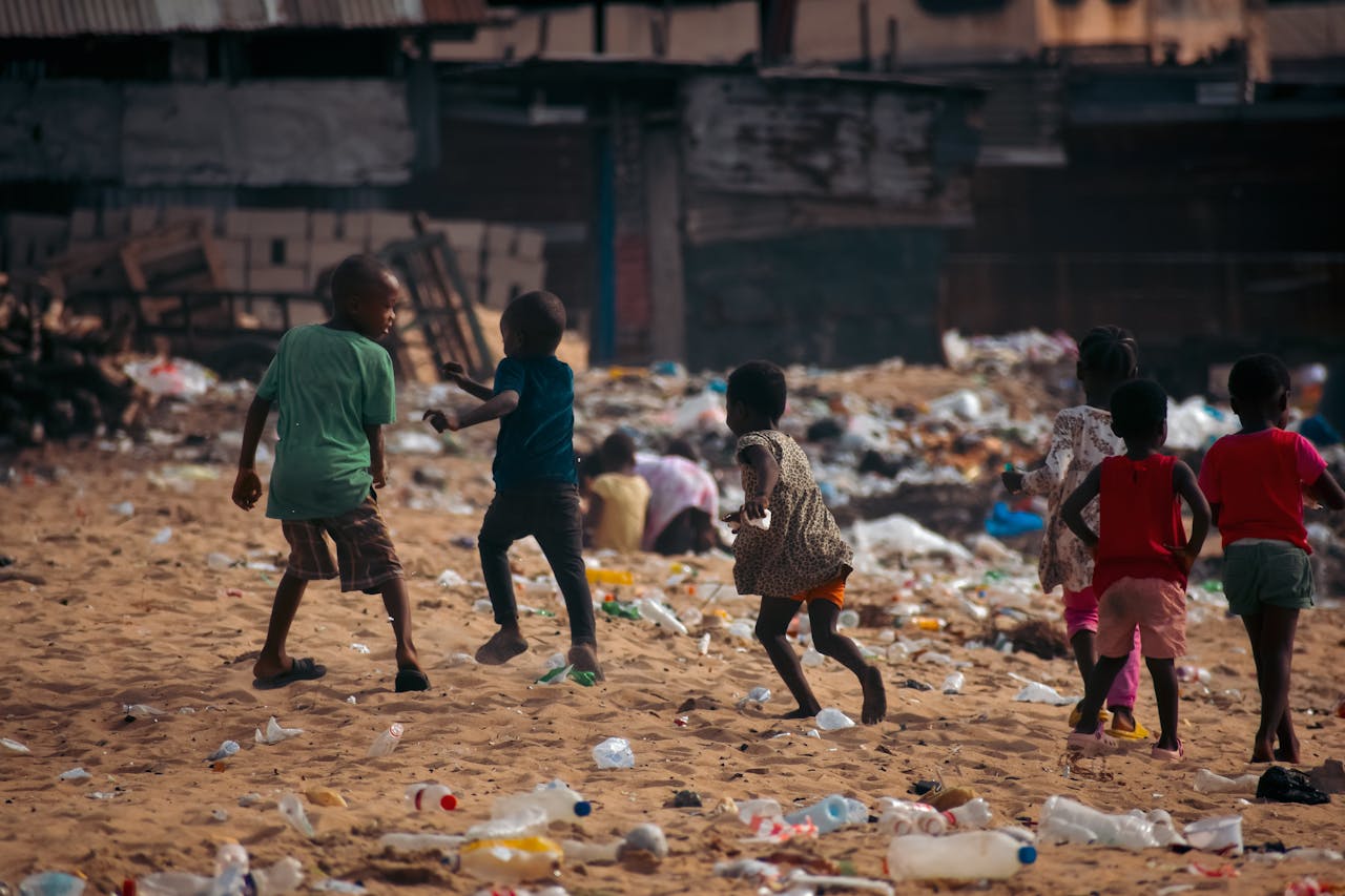 Children play on a waste-covered urban beach, highlighting pollution and climate challenges.